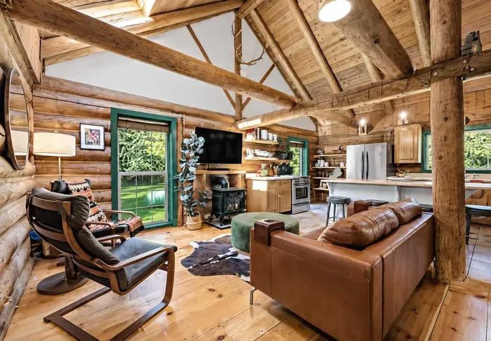 Relax in the open living area with leather seating, exposed log beams, a cozy gas fireplace, and the kitchen just beyond.