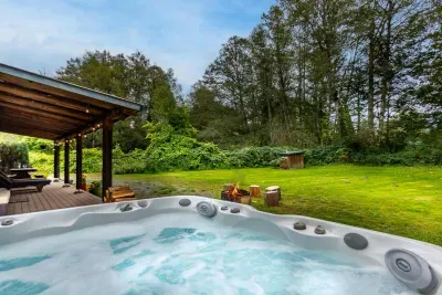 Soak in the outdoor hot tub beside the cabin, with the lawn and trees stretching out beyond the deck.