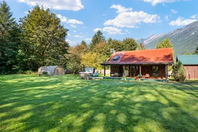 A wide daytime view of the cabin and spacious lawn, surrounded by trees with mountains beyond.