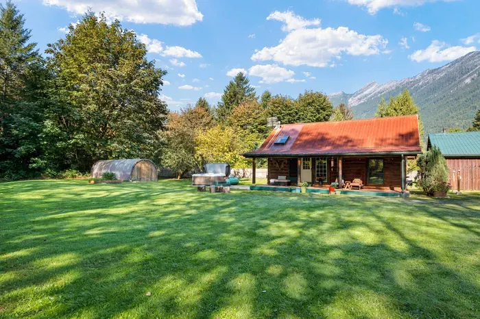 A wide daytime view of the cabin and spacious lawn, surrounded by trees with mountains beyond.