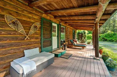 The covered porch runs along the log cabin, offering sheltered seating and space to enjoy the outdoors.