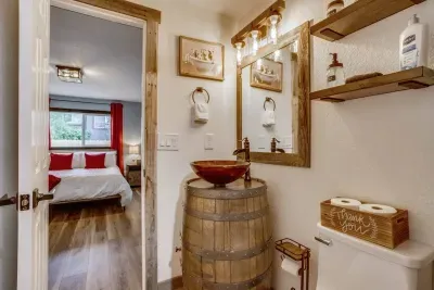 Master bathroom: Custom barrel vanity with sink bowl and a spicket faucet. Extra toilet paper, lotion, Q-tips, cotton pads, floss, hand soap, hand towel, custom framed mirror, and rustic vanity lights.