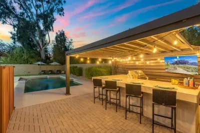 Covered grill area with gas grill, mini fridge, bar seating and string lights. Drinks not included.