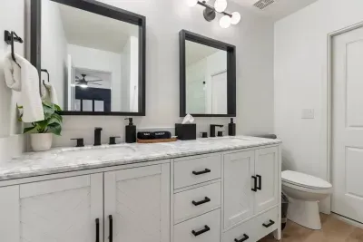 The modern primary bathroom features sleek white tiles, contemporary fixtures, and a vanity with a hair dryer and straightener. A private door leads to the backyard pool area.