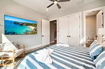Relax in this inviting bedroom featuring a plush bed, coastal accents, and a large TV for unwinding. Enjoy easy access to an en-suite bath and unwind in comfort after a day of sun, sand, and seaside adventures!