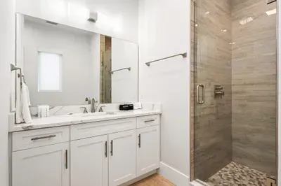 Modern bathroom featuring a sleek glass walk-in shower with stone accents and a bright vanity with ample counter space. Fresh, contemporary design makes it a comfortable and stylish place to get ready or unwind.