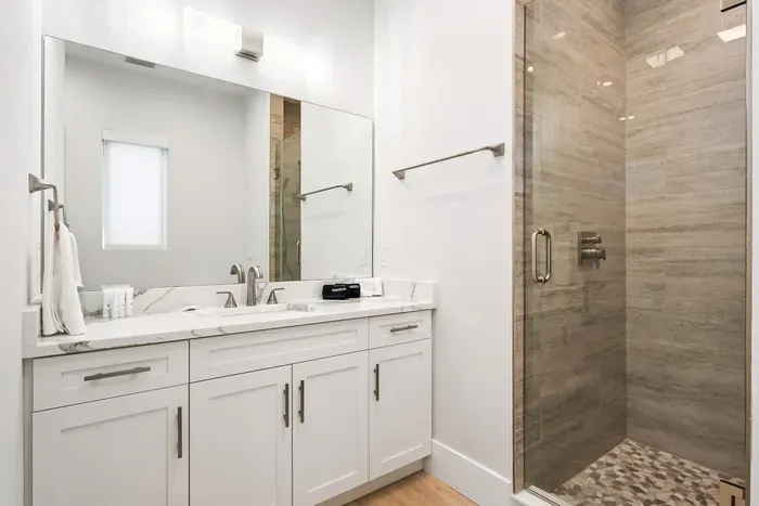 Modern bathroom featuring a sleek glass walk-in shower with stone accents and a bright vanity with ample counter space. Fresh, contemporary design makes it a comfortable and stylish place to get ready or unwind.