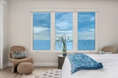 Wake up to calming sea views framed by large windows in this bright, coastal-inspired bedroom. Soft décor and natural light create the perfect retreat.