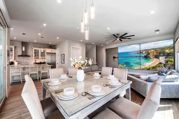 Gather in this bright, open-concept living space featuring a stylish dining area, modern kitchen, and cozy lounge with large TV. Elegant décor, ample seating, and natural light create the perfect setting for meals, relaxation, and memorable stays!