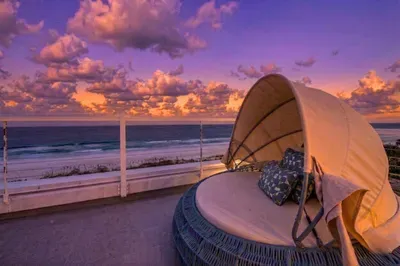 Unwind in a luxurious outdoor lounge as the sun sets over the ocean, painting the sky in vibrant hues. Cozy up in the stylish daybed, feel the sea breeze, and enjoy a serene, unforgettable beachfront escape!