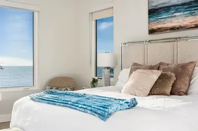 This inviting bedroom features large windows framing postcard-worthy views of the beach and water, blending relaxation with beauty.