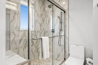 Spa-inspired bathroom with floor-to-ceiling marble, a sleek glass walk-in shower, and bright natural light. Modern fixtures create a fresh, airy space — the perfect place to refresh and rejuvenate during your stay.