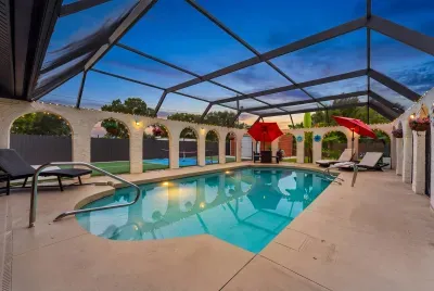 Twilight by the pool: screened lanai under decorative white arches, string lights glowing, pool uplit for an evening swim.