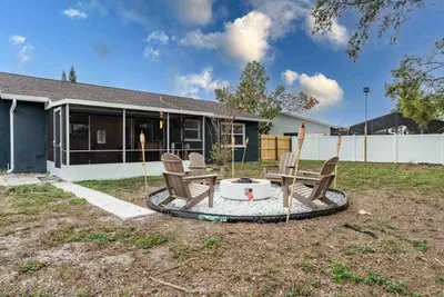 A serene outdoor space anchored by a stylish fire pit, surrounded by comfy Adirondack chairs. The gravel circle creates a cozy gathering spot, perfect for evening storytelling or stargazing, all framed by lush greenery and a privacy fence.