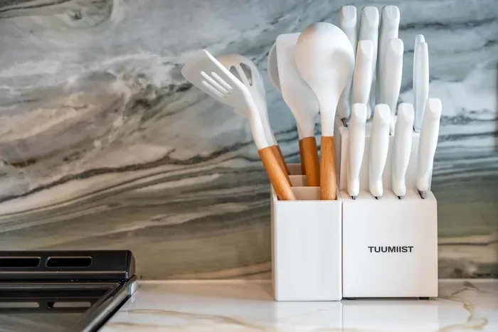 A modern utensil holder stands elegantly on the countertop, featuring a mix of minimalist white and warm wooden utensils. The sleek design perfectly complements the stunning marble backdrop, adding a touch of sophistication to the kitchen.