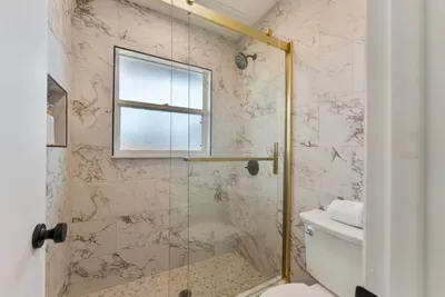 A sleek shower space showcasing a glass door and modern fixtures. Bottles of body wash, shampoo, and conditioner are neatly organized, adding convenience and style. The elegant tile work creates a serene backdrop for relaxation.