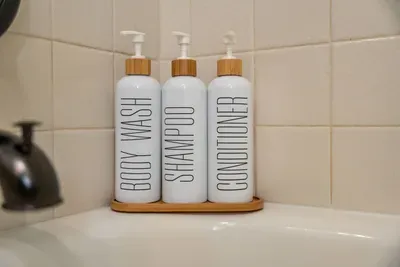 A close-up view of a well-organized shower corner featuring neatly labeled bottles for body wash, shampoo, and conditioner. The simple and clean aesthetics highlight a calming atmosphere, making it easy for guests to enjoy a relaxing bath