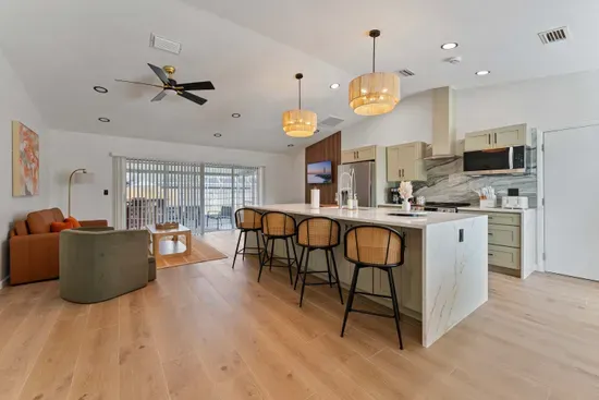 A sleek, open-concept kitchen featuring a spacious island with stunning marble countertops, flanked by stylish bar stools. The cabinetry in soft green tones complements the stainless steel appliances, and decorative light fixtures add a warm ambiance