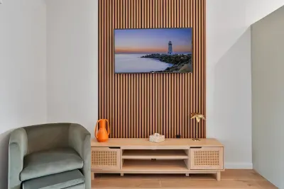 A stylish seating area with a modern couch adorned with orange accent pillows, complemented by a plush green armchair. The natural wood coffee table and a colorful piece of artwork on the wall create a warm and inviting atmosphere for relaxation.