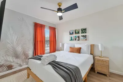 A serene bedroom featuring a comfortable queen-sized bed draped in crisp white linens and accented with an orange throw pillow.