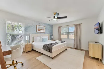 This inviting bedroom showcases a stunning ocean-inspired mural that serves as a captivating backdrop to the elegant decor. The soft bedding and stylish nightstands exude comfort, while large windows frame views of the outside