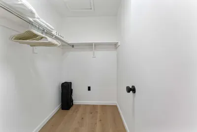 A bright and airy walk-in closet showcasing ample storage space with organized shelving and hanging options. The minimalist design and natural wood flooring provide a clean and functional area for guests to easily unpack and settle in