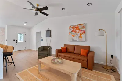 An expansive view of the living room that showcases the harmonious layout. The inviting couch, chic armchair, and colorful decor invite gatherings, while the bright lighting enhances the cozy ambiance, perfect for socializing or unwinding.