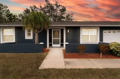 This inviting exterior showcases a beautifully maintained home, illuminated by a stunning sunset sky filled with warm hues. The landscaped front yard features green shrubbery and a palm tree