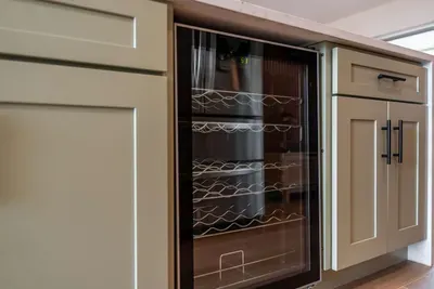 A closer look at the thoughtfully designed cabinetry reveals a sleek wine cooler, ideal for entertaining. The modern hardware and organized shelving make it easy to access essentials while maintaining a polished appearance in the kitchen.