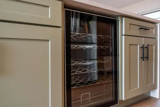 A closer look at the thoughtfully designed cabinetry reveals a sleek wine cooler, ideal for entertaining. The modern hardware and organized shelving make it easy to access essentials while maintaining a polished appearance in the kitchen.