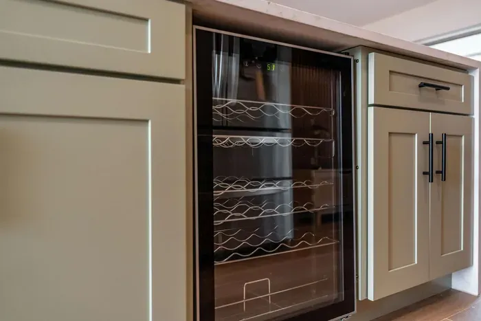 A closer look at the thoughtfully designed cabinetry reveals a sleek wine cooler, ideal for entertaining. The modern hardware and organized shelving make it easy to access essentials while maintaining a polished appearance in the kitchen.