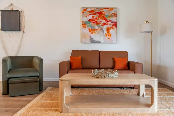 A beautifully decorated entertainment area highlighting a stunning piece of coastal art on the wall. The sleek TV setup and soft furnishings create a sophisticated space, inviting guests to enjoy both comfort and style.