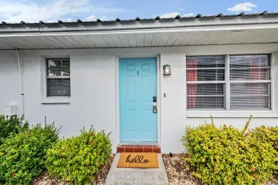 Charming entryway with a cheerful blue door, welcoming doormat, and manicured greenery. This bright, inviting exterior sets the perfect tone for your relaxing coastal getaway.