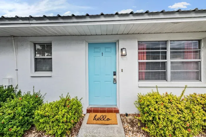 Charming entryway with a cheerful blue door, welcoming doormat, and manicured greenery. This bright, inviting exterior sets the perfect tone for your relaxing coastal getaway.