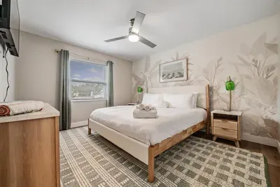 Serene bedroom retreat featuring a plush king bed, soft natural tones, and a calming mural accent wall. Enjoy ample light, cozy textures, and a peaceful ambiance—perfect for unwinding and recharging in comfort.