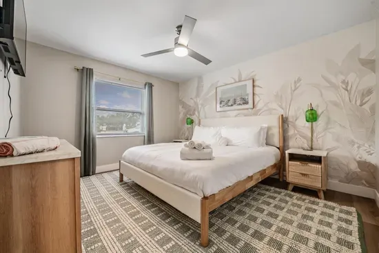 Serene bedroom retreat featuring a plush king bed, soft natural tones, and a calming mural accent wall. Enjoy ample light, cozy textures, and a peaceful ambiance—perfect for unwinding and recharging in comfort.