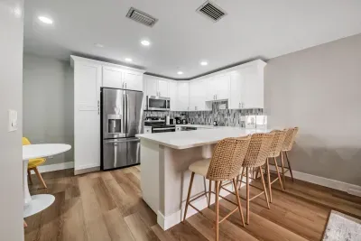 Modern kitchen with stainless appliances, spacious quartz island, and stylish wicker barstools. Perfect for cooking, dining, and gathering—this bright, open space blends convenience and coastal charm effortlessly