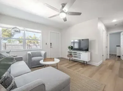 Cozy and modern living area featuring a plush sectional, flat-screen TV, and stylish décor. Bright windows fill the room with natural light, creating a relaxed, airy atmosphere perfect for lounging or movie nights.