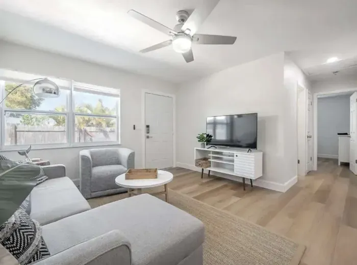 Cozy and modern living area featuring a plush sectional, flat-screen TV, and stylish décor. Bright windows fill the room with natural light, creating a relaxed, airy atmosphere perfect for lounging or movie nights.