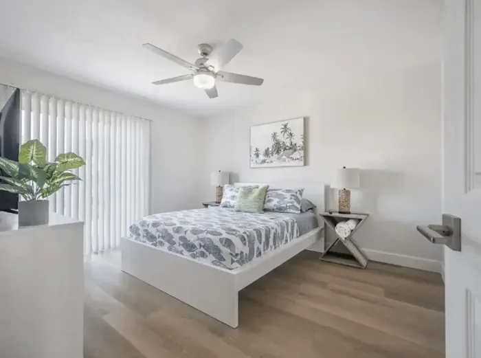 Bright and airy bedroom featuring a plush queen bed, crisp linens, and calming coastal tones. Large windows fill the space with natural light, while modern décor and sleek flooring create a relaxing, contemporary retreat.
