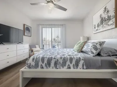 Serene bedroom with a cozy queen bed, soft coastal décor, and natural light streaming through sliding doors. Features a flat-screen TV, modern furnishings, and a private balcony view—perfect for unwinding after a sun-filled day.