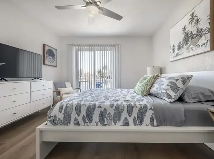 Serene bedroom with a cozy queen bed, soft coastal décor, and natural light streaming through sliding doors. Features a flat-screen TV, modern furnishings, and a private balcony view—perfect for unwinding after a sun-filled day.