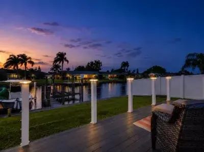Twilight canal-side deck with glowing post-cap lights, peaceful waterfront views, and cozy outdoor seating. Unwind by the water, watch boats pass by, and enjoy the calm coastal atmosphere after sunset.