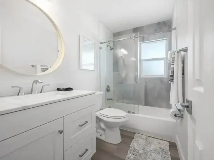 Modern and elegant bathroom with sleek white cabinetry, a glass-enclosed shower-tub combo, and stylish gray tile accents. Bright lighting and clean design create a spa-like space perfect for refreshing and unwinding.