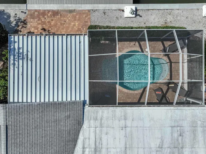 Take in the breathtaking top view of the property, where you can spot the sparkling pool through the lanai screen. This picturesque perspective showcases the perfect blend of outdoor relaxation and tropical beauty, offering an ideal retreat for you.