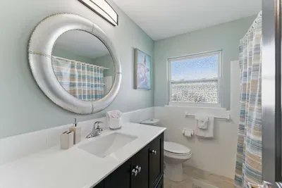 This modern bathroom features a clean and spacious toilet area, complemented by a wide round mirror that adds a touch of elegance and spaciousness to the room.