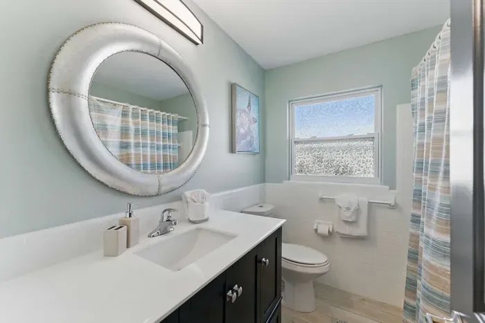 This modern bathroom features a clean and spacious toilet area, complemented by a wide round mirror that adds a touch of elegance and spaciousness to the room.