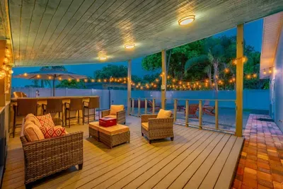 Charming covered patio with cozy wicker seating, glowing string lights, and bar area—perfect for evening cocktails or morning coffee. Relax and unwind while enjoying a warm, inviting ambiance that flows seamlessly into the outdoor firepit lounge.