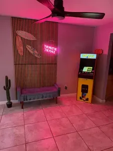Fun and vibrant game nook featuring neon lighting, surfboard décor, and a retro arcade machine! Perfect for playful nights in or photo-worthy moments—this lively space adds a cool, beachy vibe with a touch of nostalgia and modern flair.