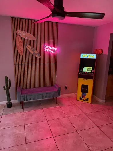 Fun and vibrant game nook featuring neon lighting, surfboard décor, and a retro arcade machine! Perfect for playful nights in or photo-worthy moments—this lively space adds a cool, beachy vibe with a touch of nostalgia and modern flair.